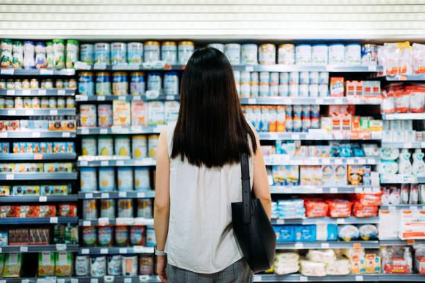 Woman looking over choices of baby formula on store shelves.