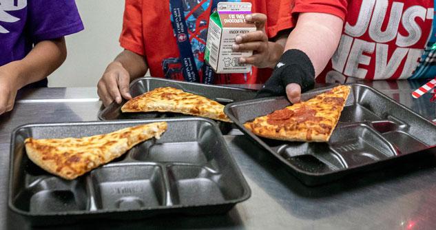 Trays of pizza with students in the background