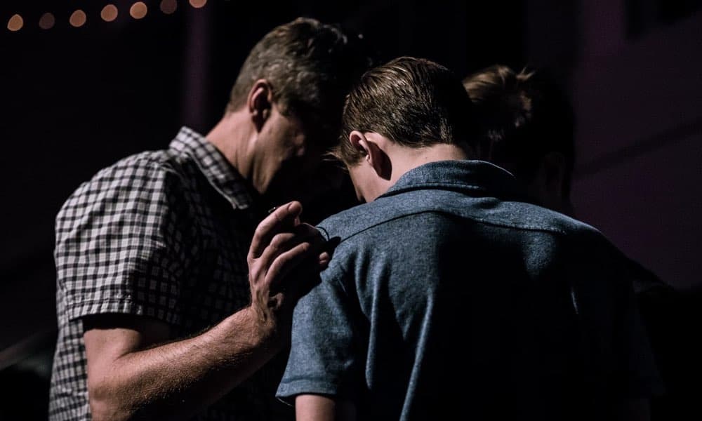 two men with heads bowed together praying