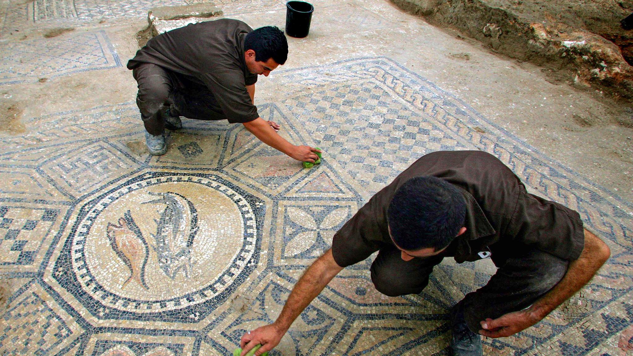 Two men carefully restoring an ancient mosaic.