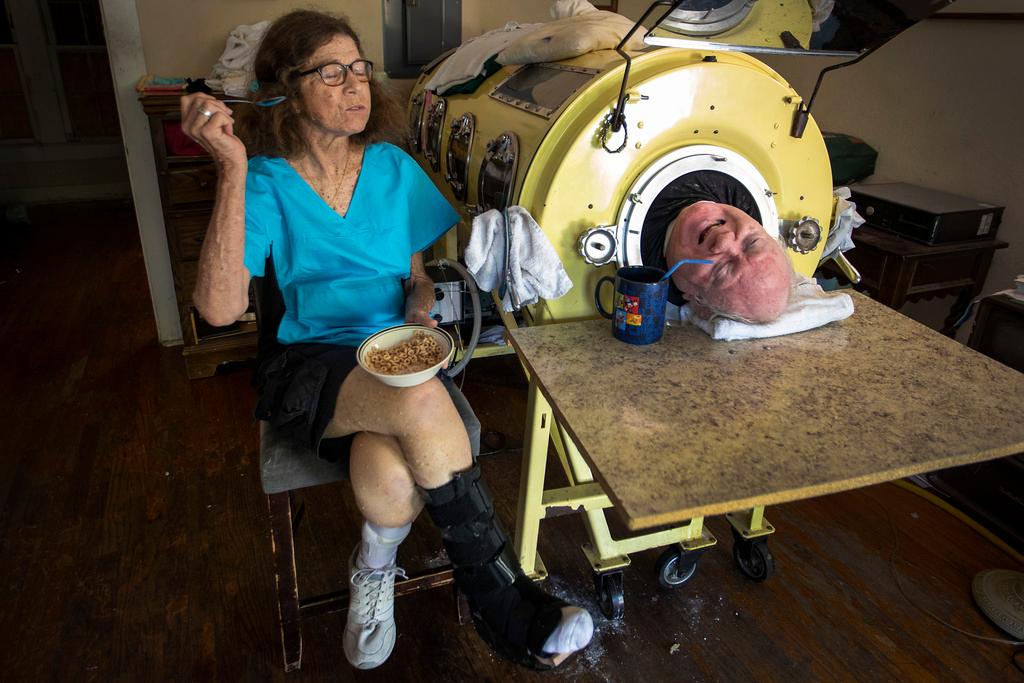 Attorney Paul Alexander chats with caregiver and friend Kathryn Gaines as he drinks coffee and she eats breakfast beside his iron lung at his home in Dallas.