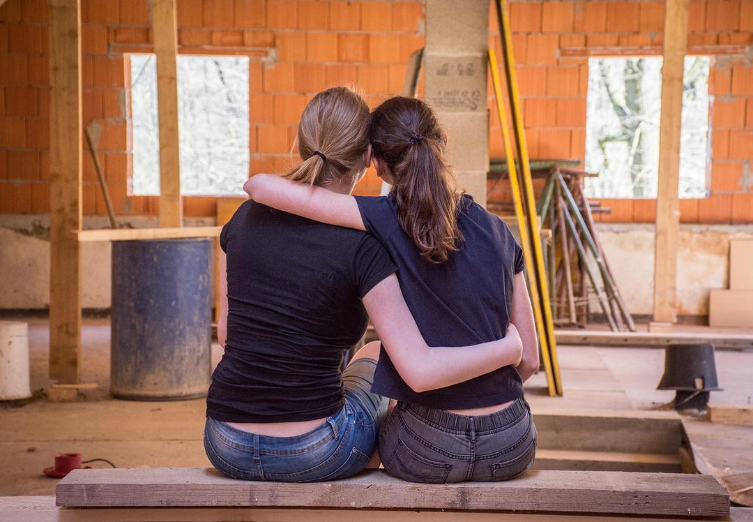 Two women from back picture watching under construction room and hugging 