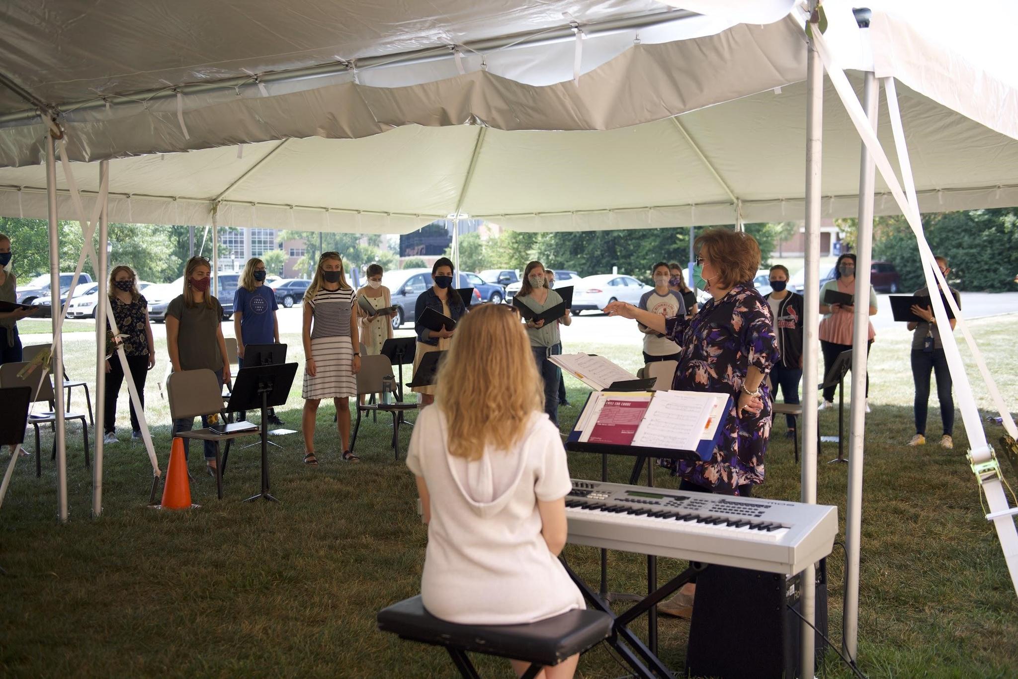 Beth Porter, department chair and associate professor of vocal music, conducts the Women’s choir during an outdoor rehearsal underneath the new tents