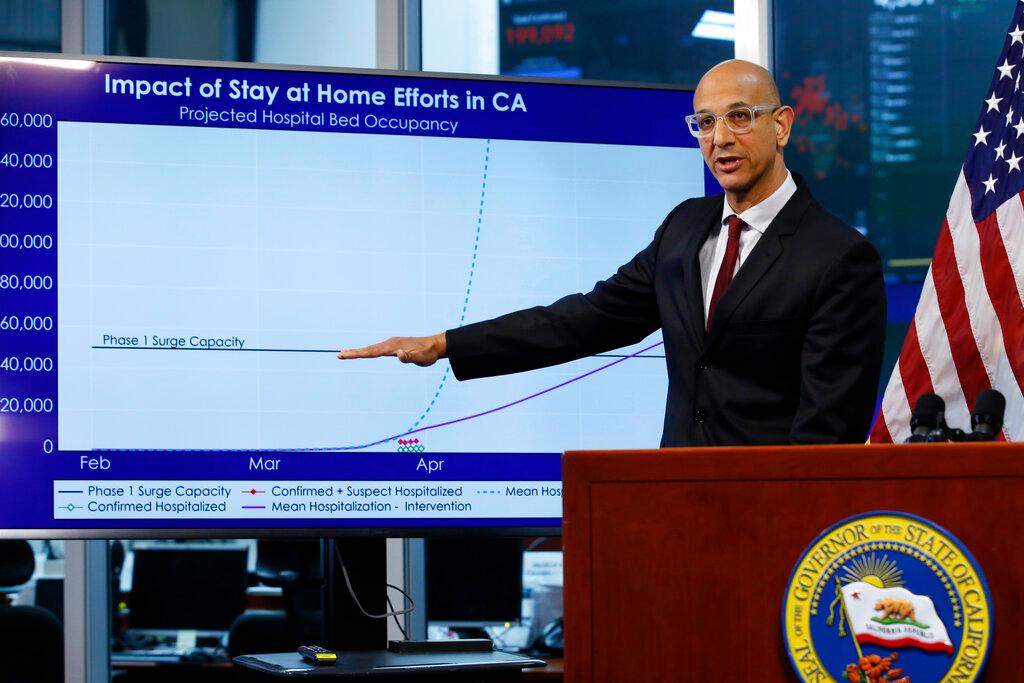 In this April 1, 2020, file photo Dr. Mark Ghaly, secretary of the California Health and Human Services, gestures to a chart showing the impact of the mandatory stay-at-home orders during a news conference ,at the Governor's Office of Emergency Services in Rancho Cordova, Calif. On Saturday, California will impose another, partial overnight curfew to stem a recent surge in coronavirus cases. Ghaly said that about 12% of the new cases will be hospitalized in coming weeks, and the cumulative increase could soon threaten to swamp the state's healthcare system as it has in other states. The curfew will run from 10 p.m. to 5 a.m.