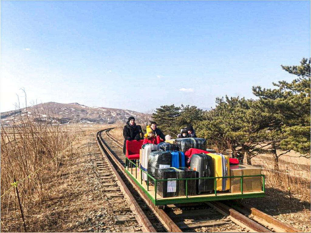 Group of Russian diplomats push hand-pushed rail trolley with their children and suitcases to the border with Russia