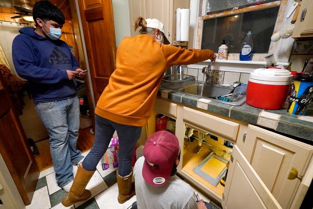 Roberto Valerio Jr., left, and his cousin Hector Valerio, right, look on as homeowner Nora Espinoza test for water coming out of the faucet