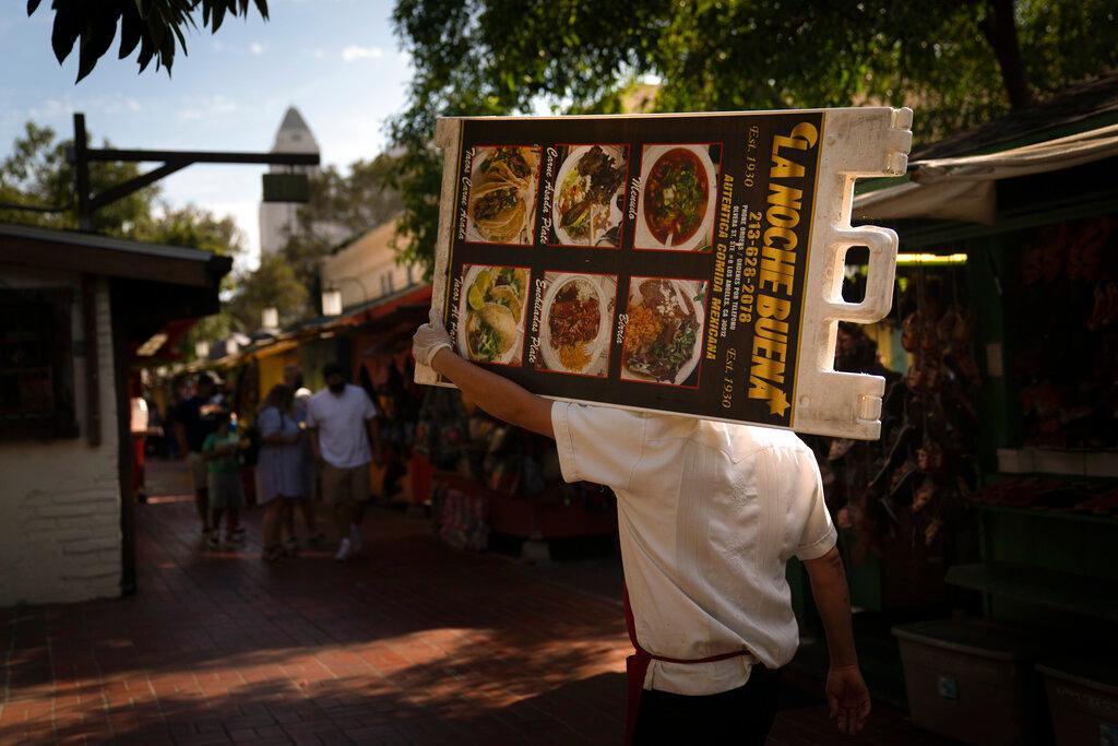 Restaurant worker Abraham Ordaz, 38, carries a menu stand along Olvera Street in Los Angeles, Tuesday, June 8, 2021. Olvera Street has long been a thriving tourist destination and a symbol of the state's early ties to Mexico. The location of where settlers established a farming community in 1781 as El Pueblo de Los Angeles, its historic buildings were restored and rebuilt as a traditional Mexican marketplace in 1930s. As Latinos in California have experienced disproportionately worse outcomes from COVID-19, so too has Olvera Street.