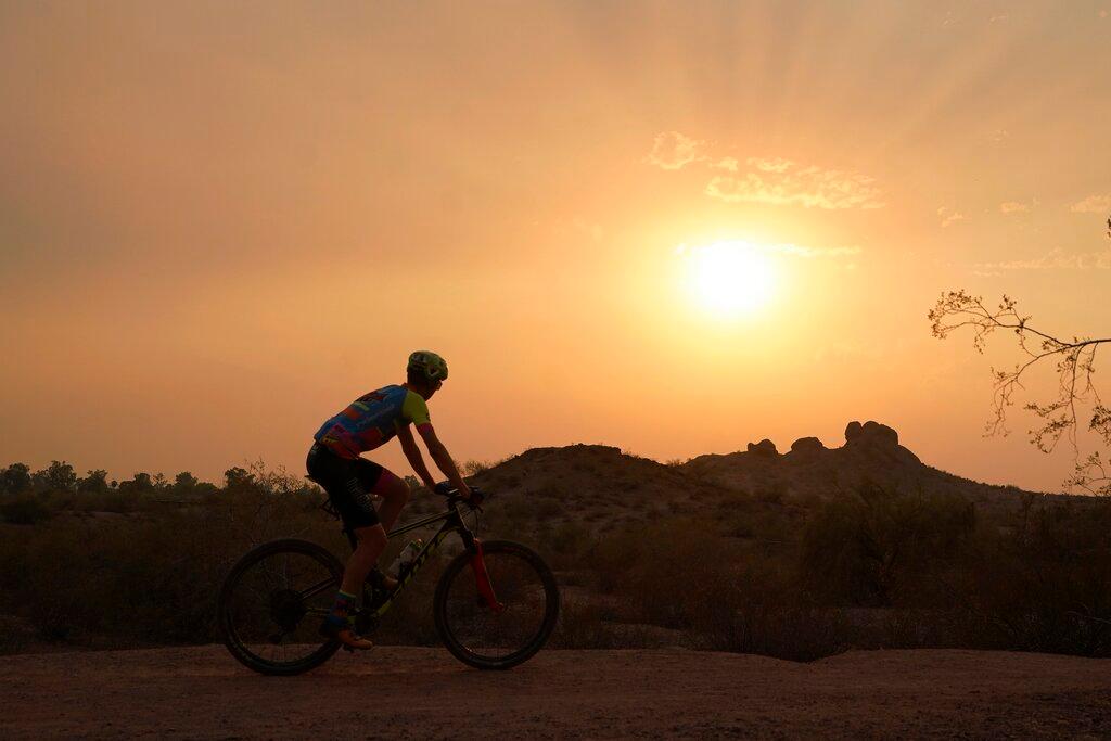 A cyclist bikes past the setting sun at Papago Park during a heatwave where temperatures hit 115-degrees in Phoenix