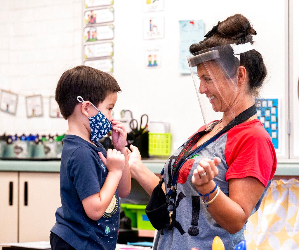 A student gets help with his mask from transitional kindergarten teacher Annette Cuccarese during the first day of classes at Tustin Ranch Elementary School in Tustin, Calif.