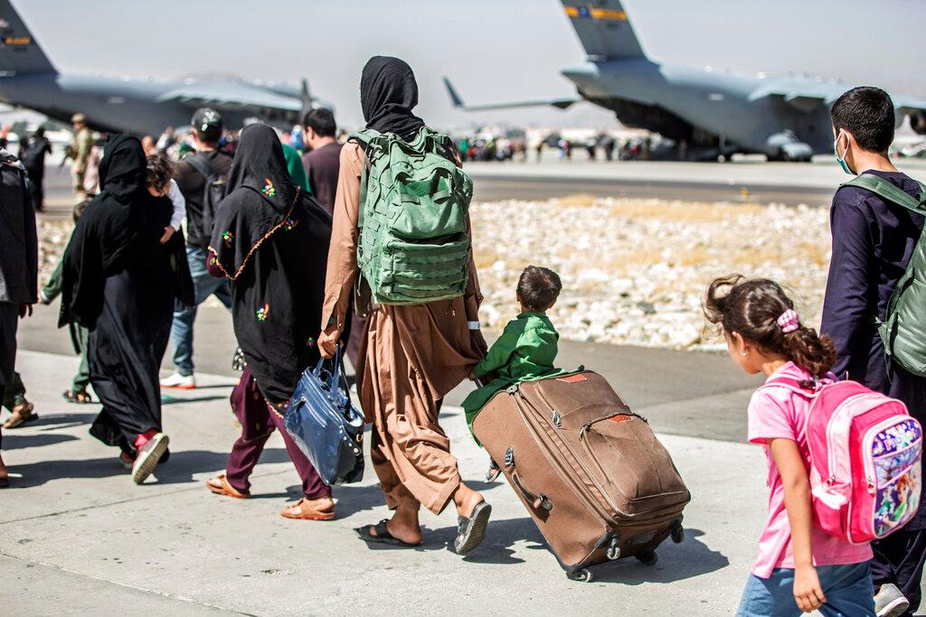 In this Aug. 24, 2021, file photo, provided by the U.S. Marine Corps, families walk towards their flight during ongoing evacuations at Hamid Karzai International Airport, in Kabul, Afghanistan. A school district in a San Diego suburb that is home to a large refugee population says many of its families who had taken summer trips to Afghanistan to see their relatives have gotten stuck there with the chaos following the withdrawal of U.S. troops.