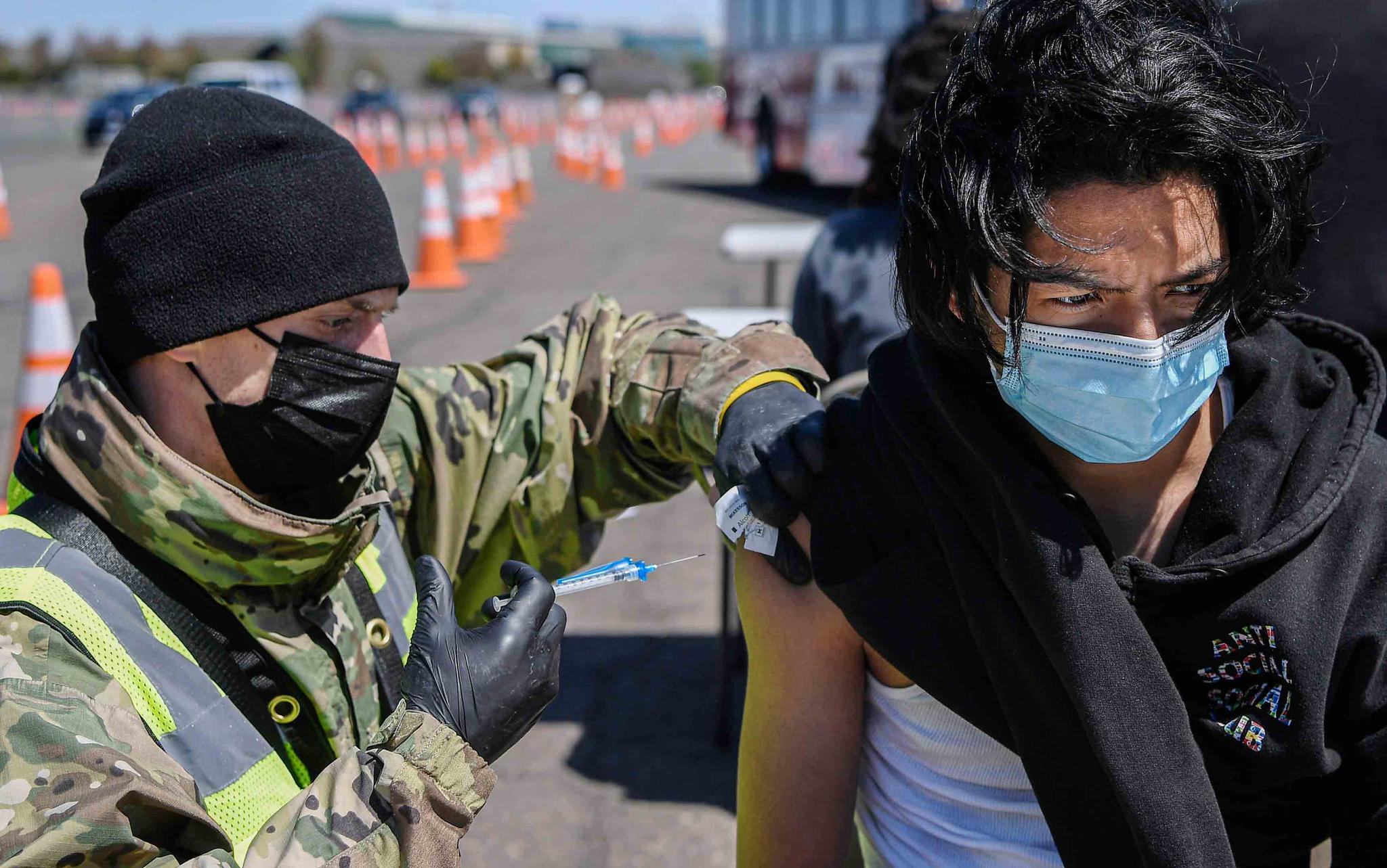 Connecticut National Guard medic Todd Smith, left, administers a shot to East Hartford High School senior Alberto Salazar Rodriguez at a mass vaccination site at Pratt & Whitney Runway in East Hartford, Conn., April 26, 2021. 
