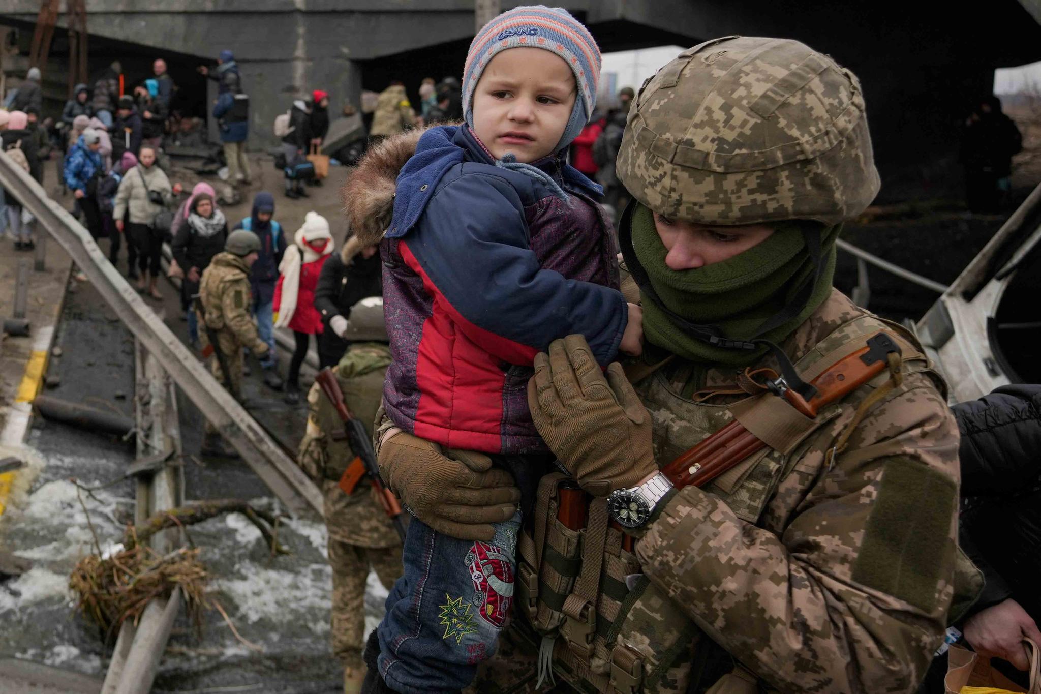 A Ukrainian serviceman holds a baby crossing the Irpin river on an improvised path under a bridge that was destroyed by a Russian airstrike, while assisting people fleeing the town of Irpin, Ukraine, Saturday, March 5, 2022.
