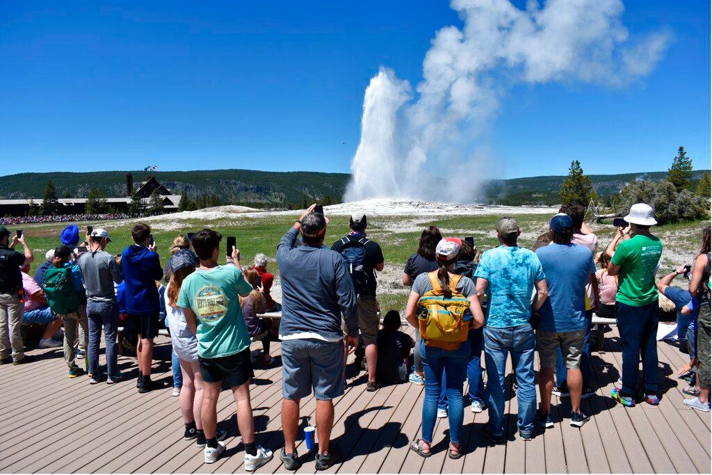 The Old Faithful geyser erupts and shoots water and steam into the air as tourists watch