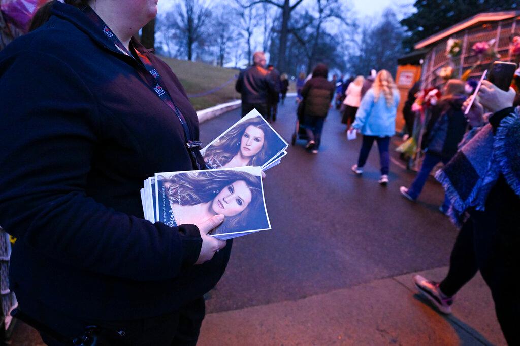 An attendant holds programs as fans enter Graceland for a memorial service for Lisa Marie Presley Sunday, Jan. 22, 2023, in Memphis, Tenn. She died Jan. 12 after being hospitalized for a medical emergency and was buried on the property next to her son Benjamin Keough, and near her father Elvis Presley and his two parents.