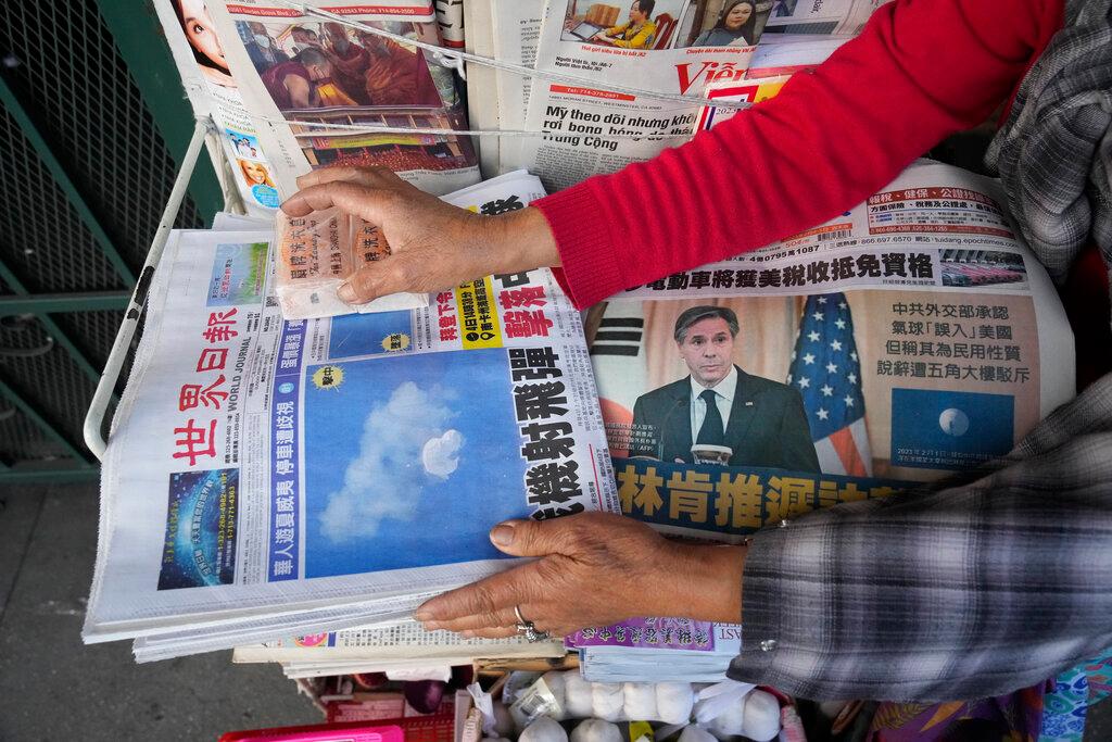 Business owner "Annie" weights down copies of the Chinese Daily News newspaper showcasing pictures of a suspected Chinese spy balloon, in the Chinatown district of Los Angeles Sunday, Feb. 5, 2023