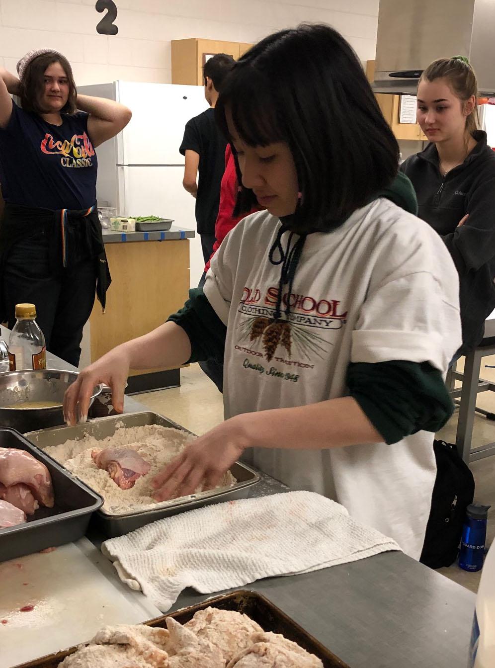 Student Mele Trinh coats chicken in batter before frying it  